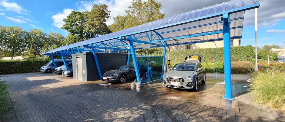 Overdekte self-carwash met blauwe stalen constructie en geparkeerde wagens